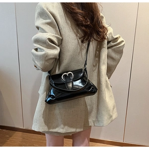 Detail of black glossy shoulder bag featuring silver heart buckle and folded pleats