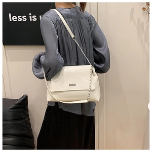 Detail of cream-colored shoulder bag featuring silver chain strap and metal logo plaque
