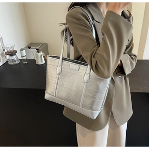 Silver tote bag with horizontal texture and gold logo plaque on a model's shoulder