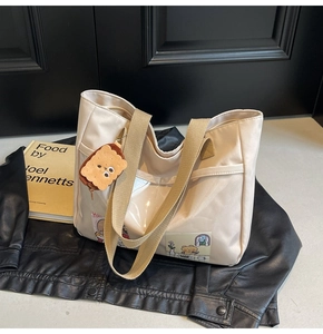 Detail of beige nylon tote bag with brown straps, cute patches and biscuit plush charm