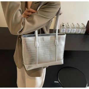 Detail of silver tote bag with horizontal texture and gold logo on beige blazer