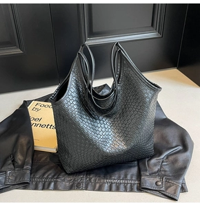 Detail of the black tote bag with woven texture placed on a stylish leather jacket background
