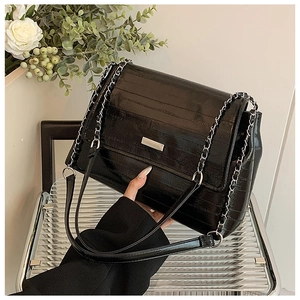 Detail of black patent leather tote bag featuring horizontal texture and silver chain strap