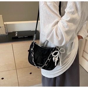 Detail of black pleated nylon bag with silver chain, pearl bow, and heart pendant