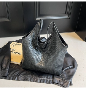 Detail of a large black tote bag with woven and crocodile texture on a leather jacket