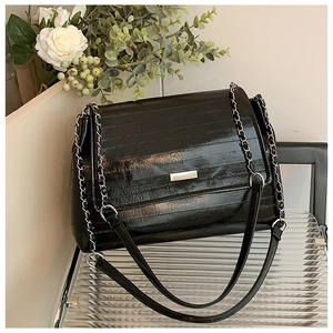 Detail of black glossy tote with horizontal embossing and silver chain strap on a chair