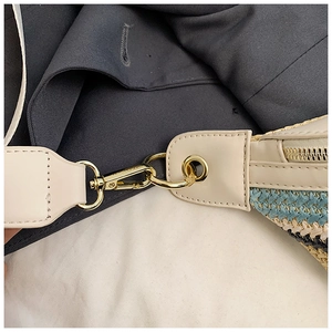 Detail der Stroh-Stofftasche mit beigem Lederriemen, goldenem Karabiner und Reißverschluss