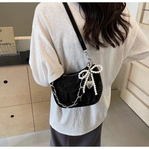 Close-up of black quilted shoulder bag with pearl bow and silver heart pendant detail