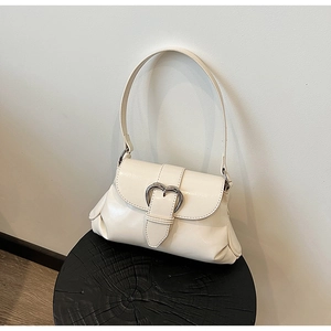 Detail of a creamy white shoulder bag featuring a large silver heart metal buckle