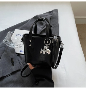 Close-up of black crossbody bucket bag with silver balloon dog charm and dual handles