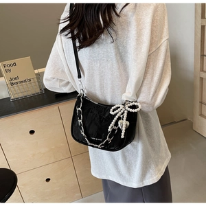 Detail of black pleated crossbody bag with pearl bow and silver heart pendant