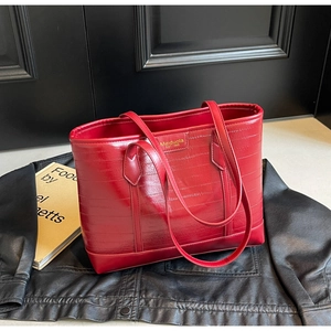 Detail of red crocodile embossed leather tote bag with gold logo on black leather background