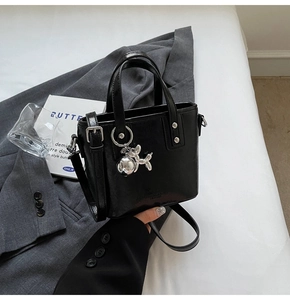 Detail of a black glossy leather bucket bag with silver balloon dog charm on a blazer