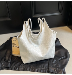 Close-up of white woven leather tote bag texture on black jacket and yellow book