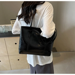 Detail view of black crocodile pattern tote bag with polished metal logo and shoulder strap