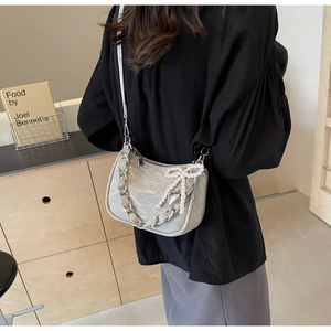 Close-up of a silver pleated shoulder bag with metal chain and pearl bow charm