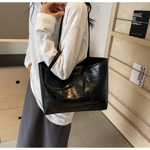 Detail of glossy black large tote bag with metallic logo on textured faux leather