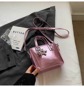 Detail of metallic purple leather bucket bag with silver charm on gray blazer