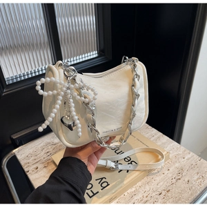 Detail of cream pleated crossbody bag with pearl bow, silver chain, and fashion text