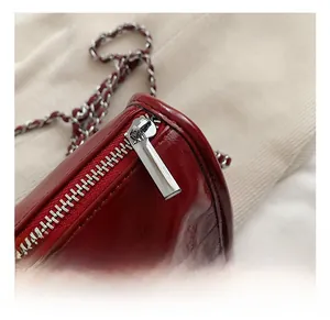 Detail of silver zipper and woven chain strap on glossy wine red leather bag