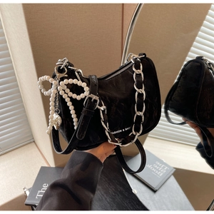 Detailed macro view of black velvet handbag with pearl bow charm and silver chain strap