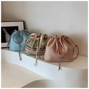 Three hand-woven straw bucket bags in blue, striped, and pink with leather drawstrings