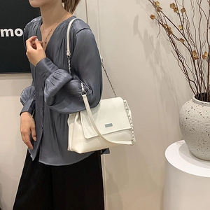 White soft leather tote bag with metal chain strap worn by a model in casual style