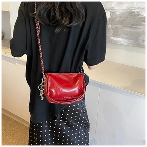 Detail of red glossy crossbody pillow bag with silver chain strap and bear charm