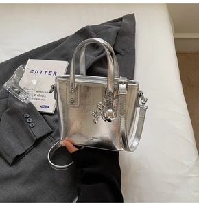 Detail of silver bucket bag with cracked texture and balloon dog charm on bed