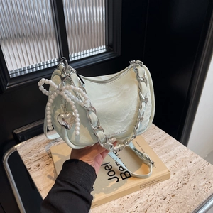 Pale mint green textured shoulder bag with silver chain and pearl bow charm on marble