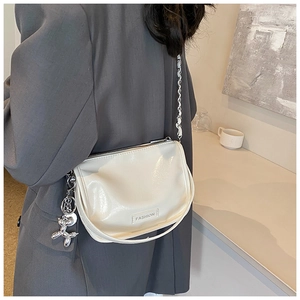 Detail of glossy cream leather crossbody bag with silver chain and balloon dog charm