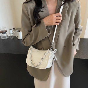 White pleated crossbody bag with chunky silver chain and pearl bow charm shown on model