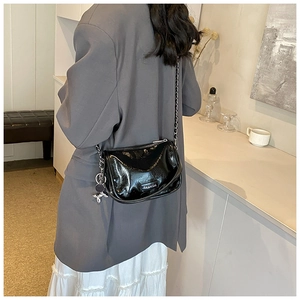 Detail of black patent leather crossbody bag with silver rabbit charm and chain strap