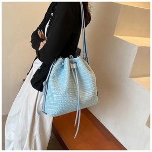 Detail of light blue woven drawstring bucket bag with textured stripes and slim strap