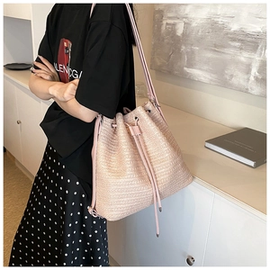 Detail view of woven straw bucket bag in light pink with drawstring closure and slim strap