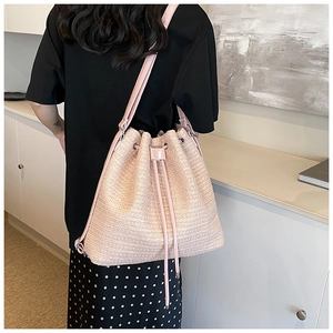 Detail of pink woven straw backpack with drawstring closure and leather straps on model