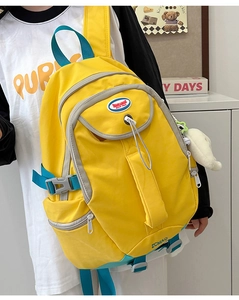 Detail of yellow nylon backpack with blue straps, external pockets and plush bunny charm