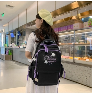 Detail of black school backpack with purple zippers and embroidery worn by a model
