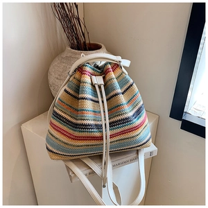 Detail of colorful striped straw bucket bag with white leather straps and drawstring