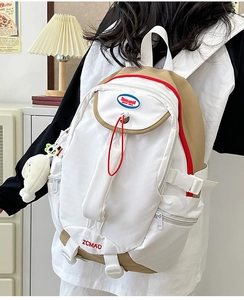 Detail of minimalist nylon backpack showing red embroidery and plush doll charm