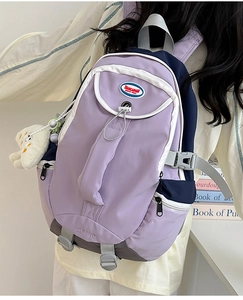 Detail view of purple nylon backpack featuring contrasting navy straps and plush toy charm
