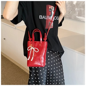 Vue détaillée du mini sac cabas en cuir verni rouge avec breloque nœud en perles