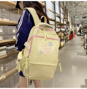Detail of light yellow canvas backpack with pink embroidery and side buckle straps