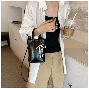 Détail d'un sac seau noir brillant avec pendentif noeud perle et bandoulière