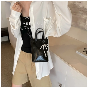 Détail d'un mini sac à main en cuir verni noir avec un pendentif nœud en perles amovible