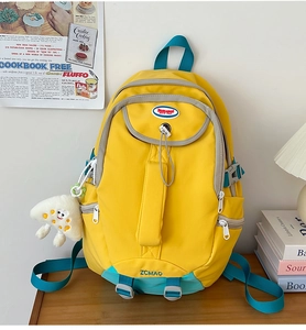 Detail of yellow nylon backpack featuring side buckle straps and a cute plush keychain