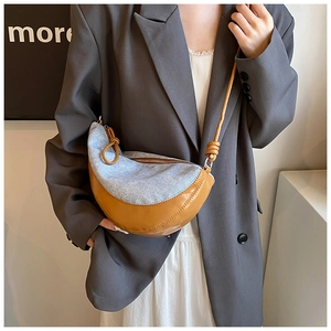 Detail of light blue denim crescent bag with brown leather trim and knotted strap detail