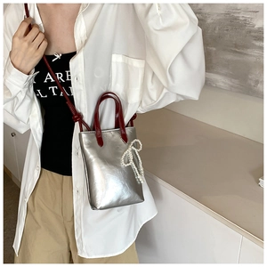 Détail du mini sac cabas argenté avec poignées bordeaux et breloque noeud en perles