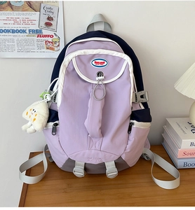 Detail of lilac and navy nylon backpack with plush charm on a wooden desk