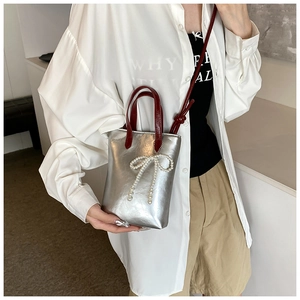 Détail du mini sac argenté avec poignées rouges et élégant accessoire de nœud en perles